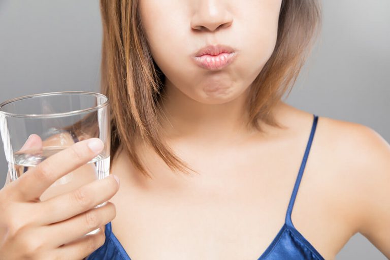 A woman holding a glass of water and swishing it in her mouth, performing an oral rinse.