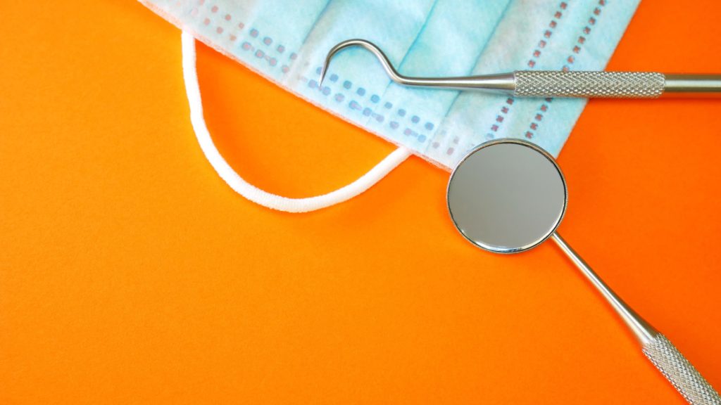 Dental tools with a mask laying on an orange background