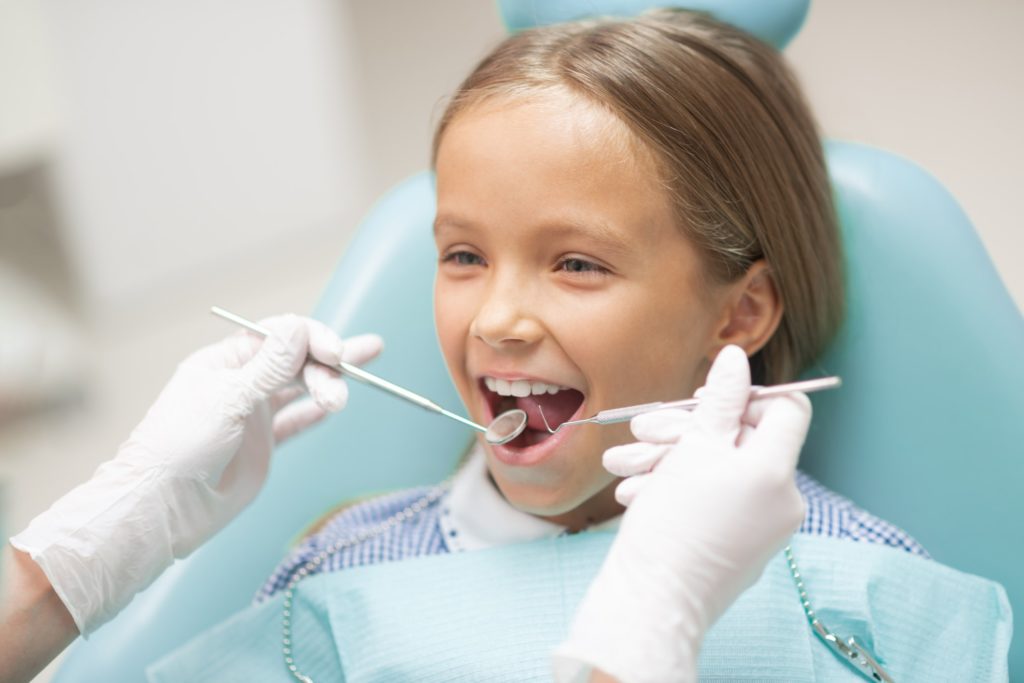 A young girl sits in a dental exam chair receiving a checkup