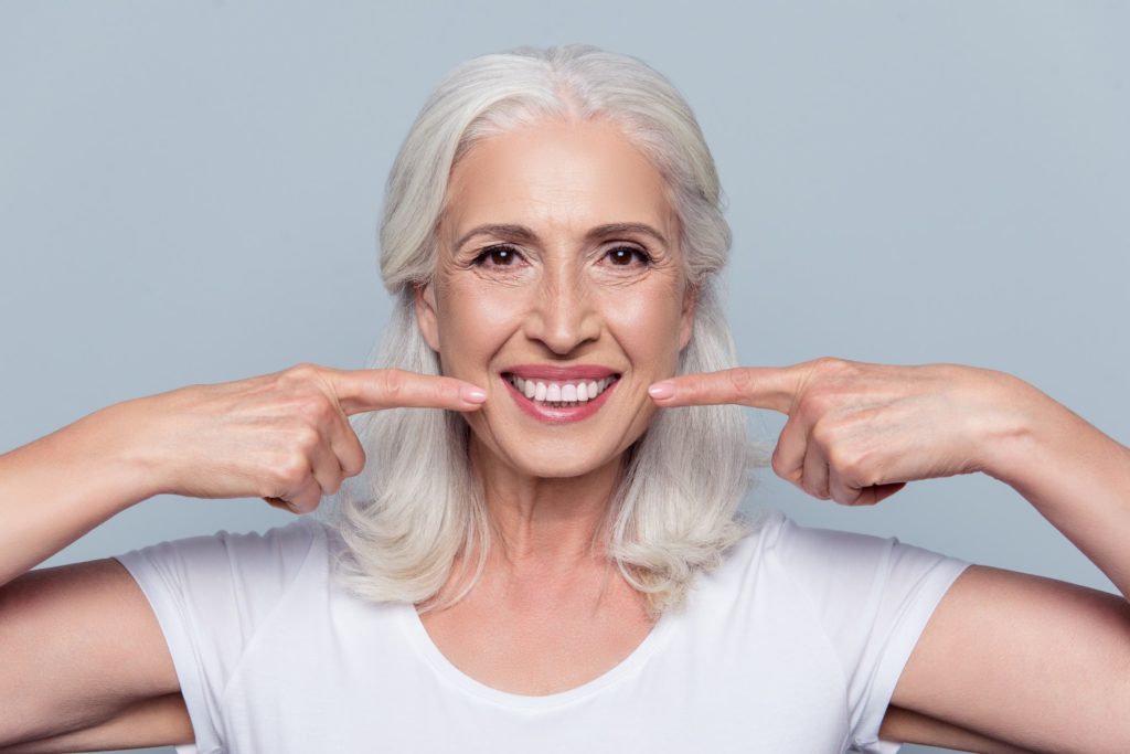 An older woman points to her white smile with both hands