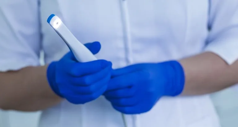 A dental professional wearing blue gloves holding an intraoral camera, used for capturing images inside a patient's mouth.