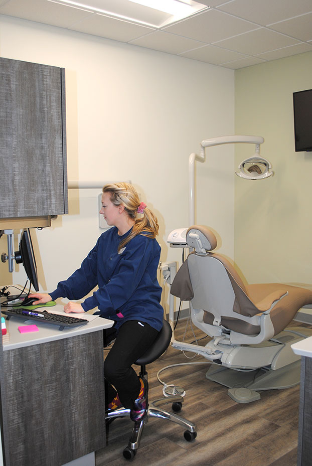A dental assistant reviews files on a monitor in an exam room