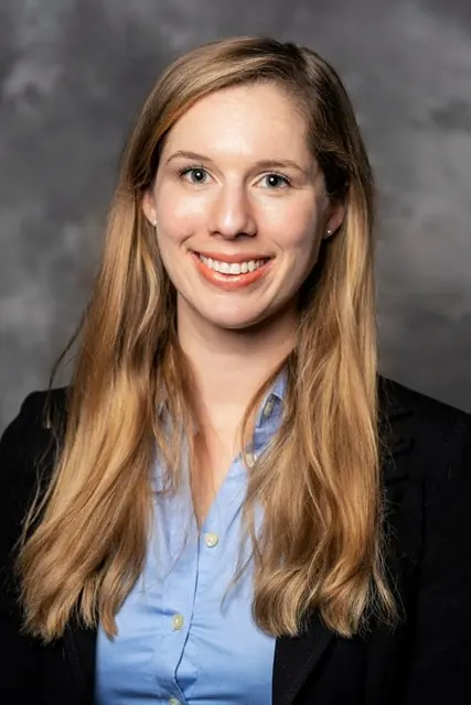 A professional headshot of Dr. Sarah Hoge, a dentist at Drum Hill Dental in Chelmsford, MA. She is wearing a blue shirt and a black blazer, smiling at the camera.