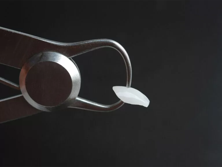 A close-up of dental tweezers holding a single dental veneer against a black background.